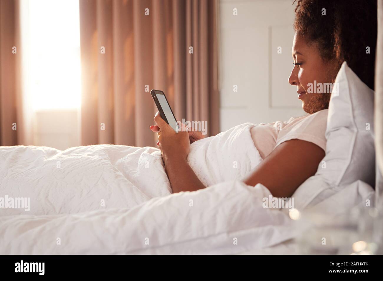 Frau sitzt oben im Bett am Handy suchen, nachdem sie aufgewacht Stockfoto