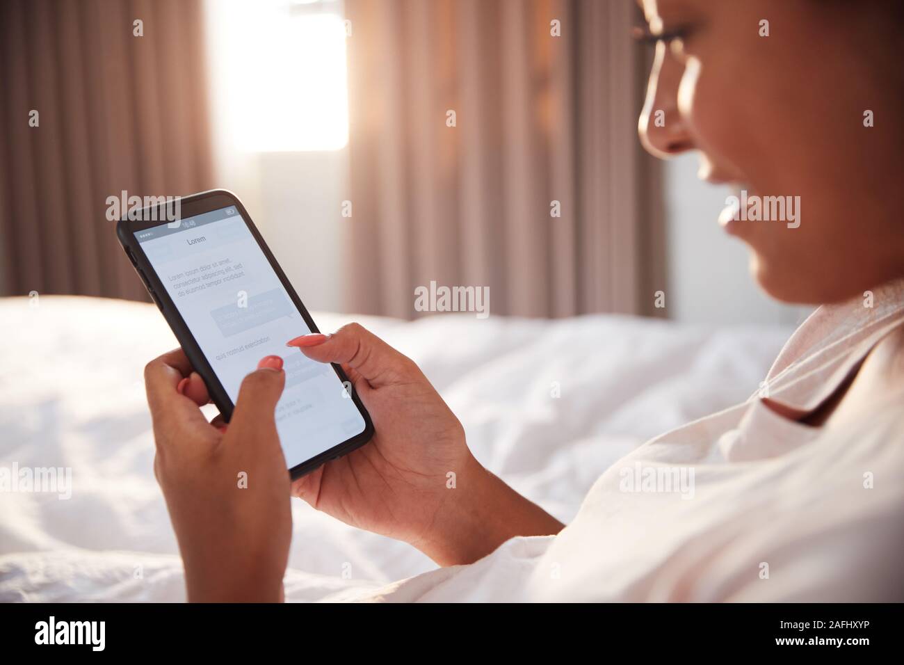 Frau sitzt oben im Bett am Handy suchen, nachdem sie aufgewacht Stockfoto