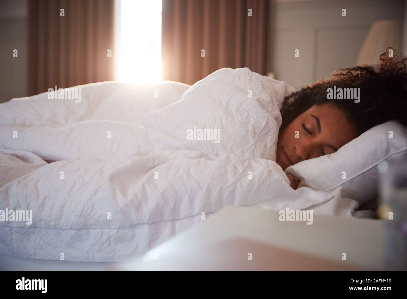 Friedliche Frau schlafend im Bett als Tag Pause durch Vorhänge Stockfoto