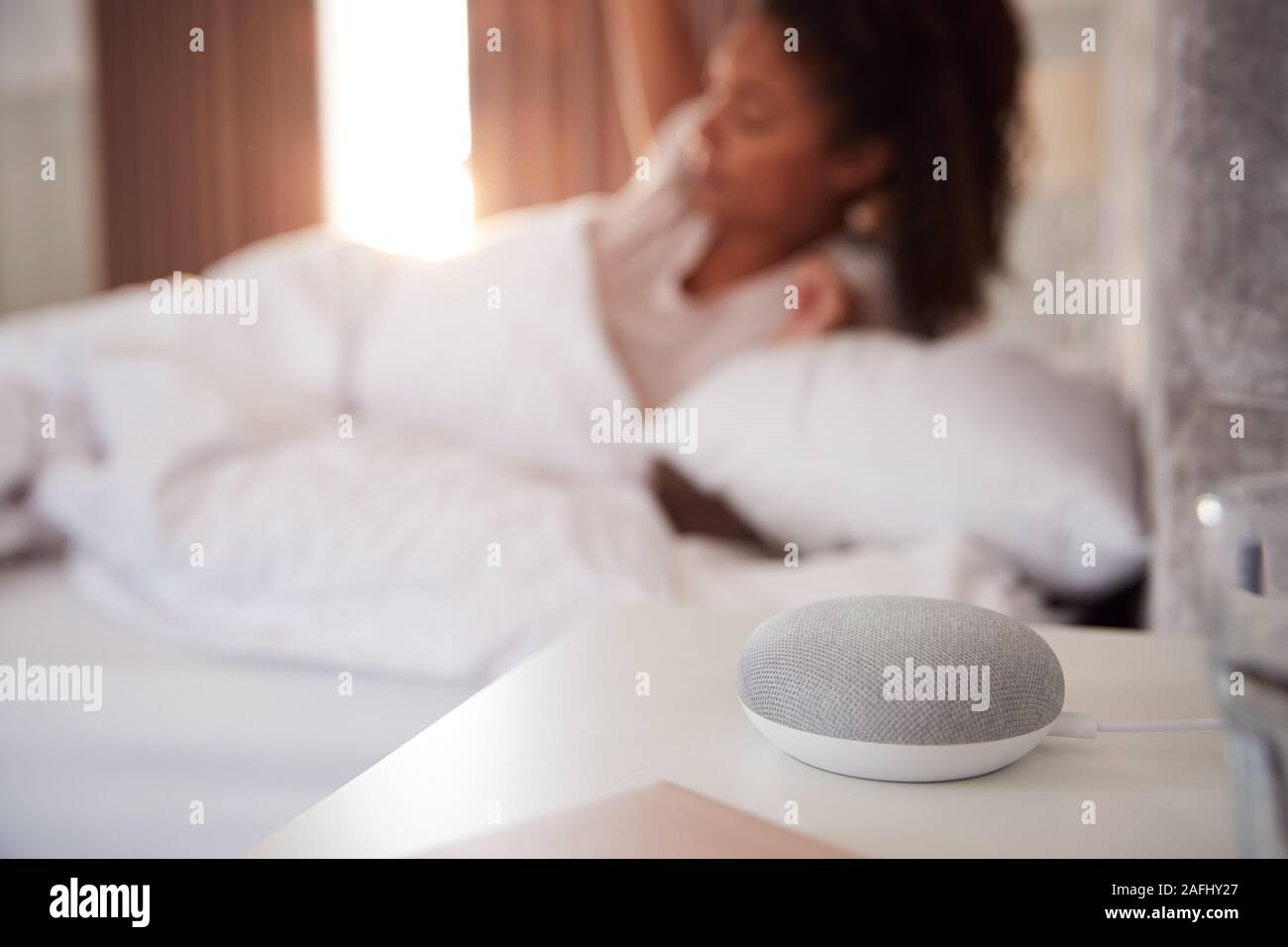 Frau Aufwachen im Bett mit Voice Assistant auf dem Nachttisch neben ihr Stockfoto