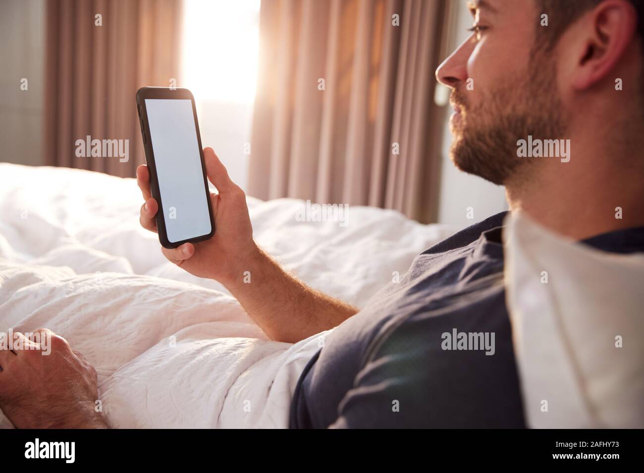 Mann sitzt im Bett am Handy suchen, nachdem sie aufgewacht Stockfoto