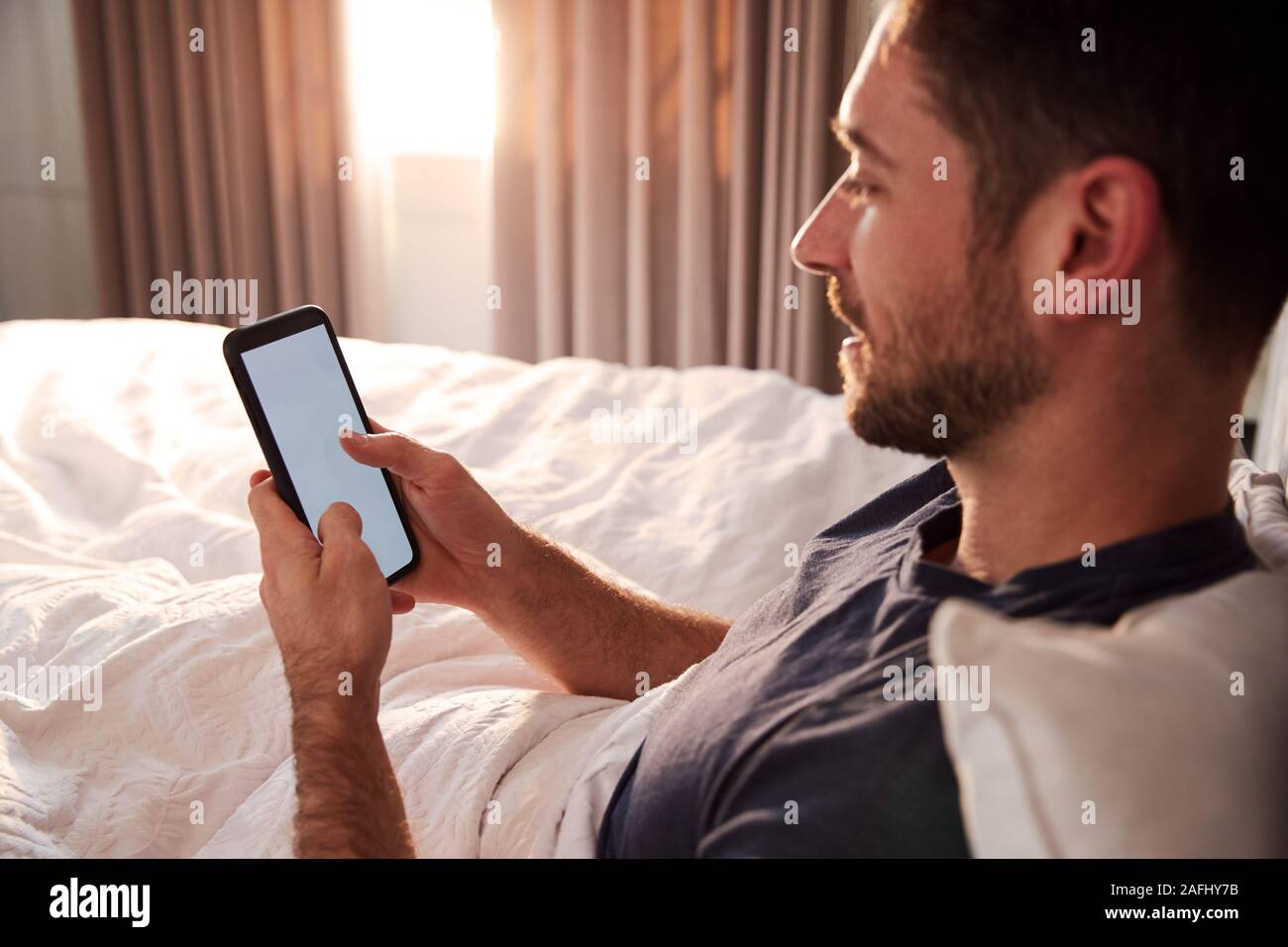 Mann sitzt im Bett am Handy suchen, nachdem sie aufgewacht Stockfoto