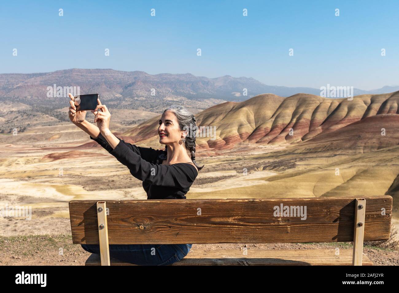 Eine junge Brünette mit grauen Strähnen macht selfies sitzen auf einer Bank in Painted Hills mit Blick auf Stockfoto