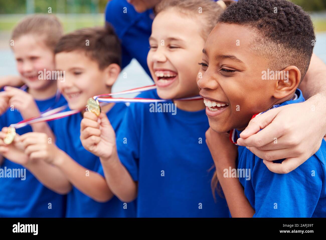 Kinder mit männlichen Trainer zeigen, ein Sieger Medaillen auf Sport Tag Stockfoto