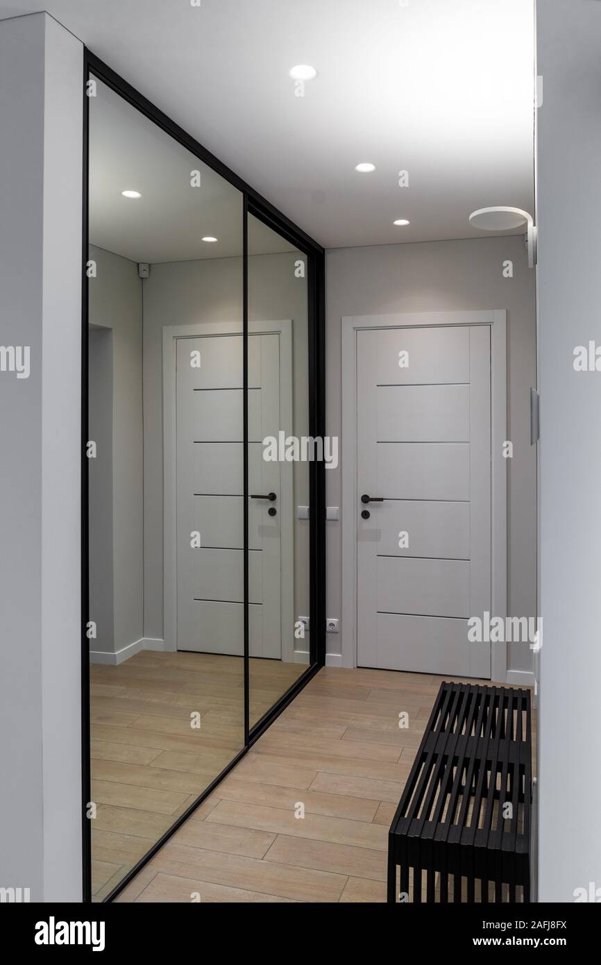 In den Korridor eines Wohnhauses. Es gibt eine Tür am Ende des Raumes, auf der rechten Seite - eine schwarze Sitzbank, auf der linken Seite - Kleiderschrank mit Spiegel Stockfoto