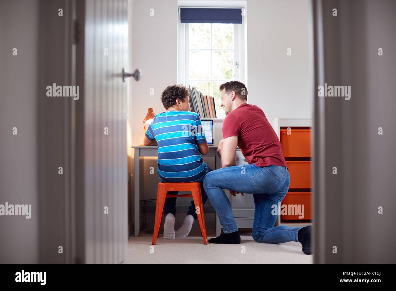 Blick durch die Tür als Vater hilft Sohn mit Laptop auf dem Schreibtisch zu tun Hausaufgaben Stockfoto