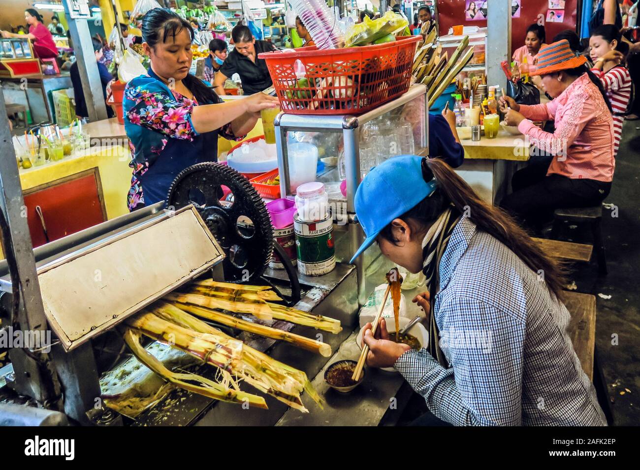 Frau, die im Zuckerrohr-Getränkestall auf dem geschäftigen Zentralmarkt dieser alten französischen Kolonialhafenstadt, Kampot, Kambodscha, isst Stockfoto