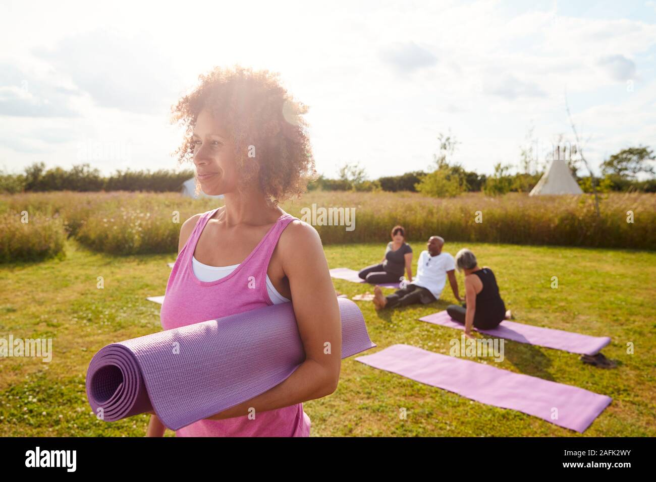 Reife Frau auf Outdoor Yoga Retreat mit Freunden und Campingplatz im Hintergrund Stockfoto