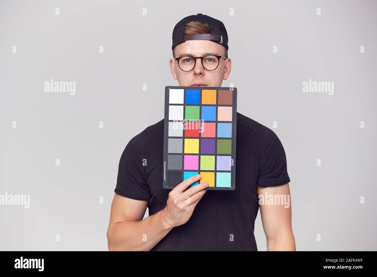 Portrait von männlichen Fotografen im Studio Holding Color Checker Karte vor weißem Hintergrund Stockfoto