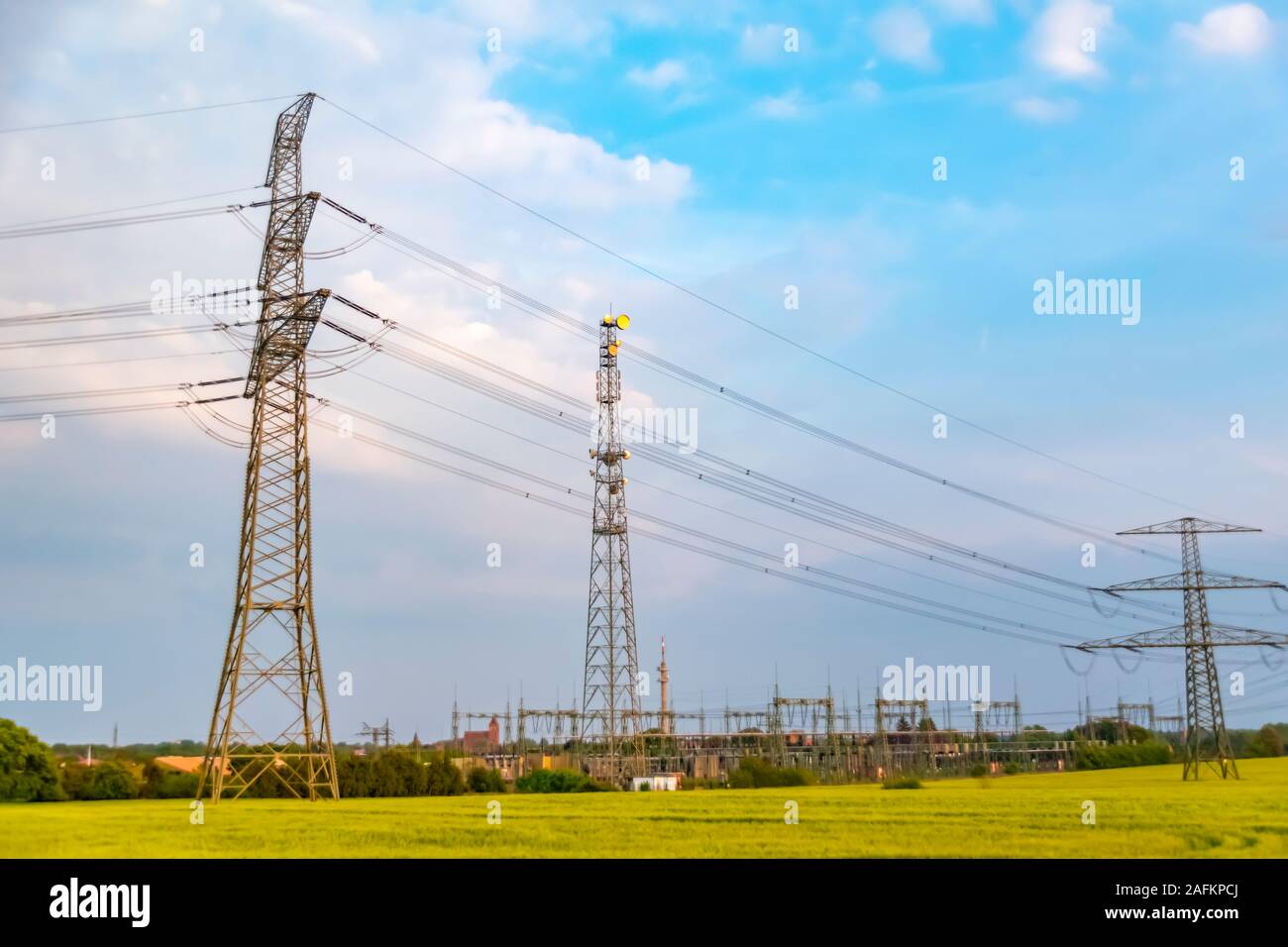 Strommasten auf einer Wiese in Deutschland. Hinter dem Umspannwerk sehen Sie ein kleines Dorf. Stockfoto