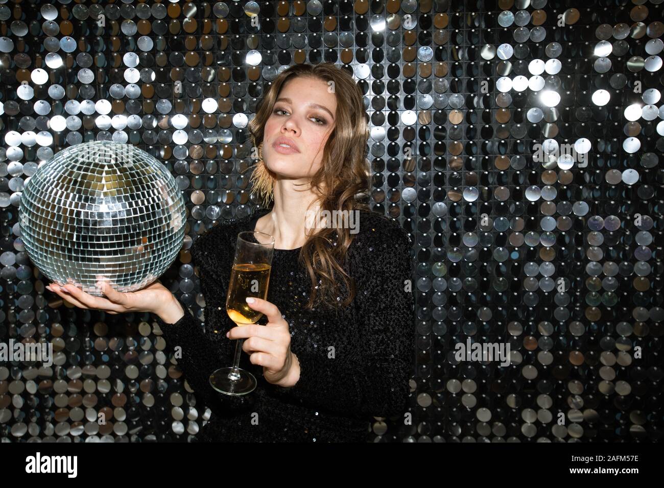 Hübsche, junge Frau mit Flöte Champagner und Disco ball Schiebeschalter an der Partei Stockfoto