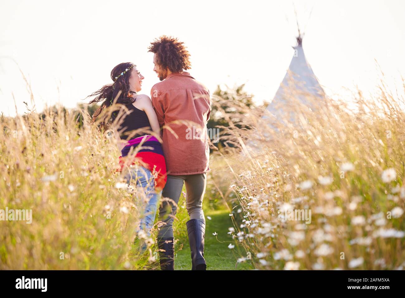 Junge romantische Paar durch das Feld in Richtung Teepee auf Sommer Camping Ferienhäuser Stockfoto