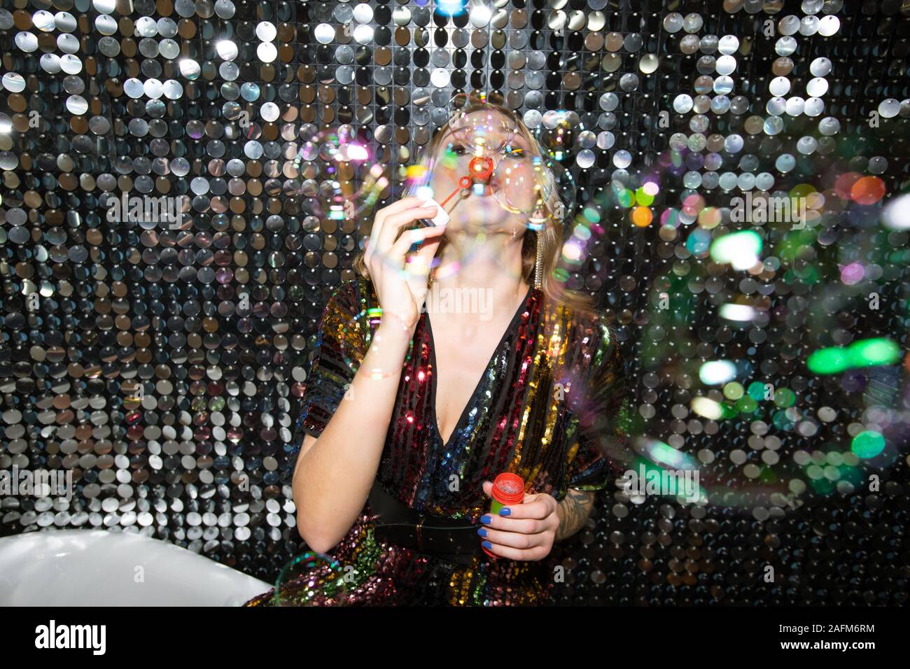 Jungen Frau im glitzernden Kleid bläst Seifenblasen bei Party Stockfoto