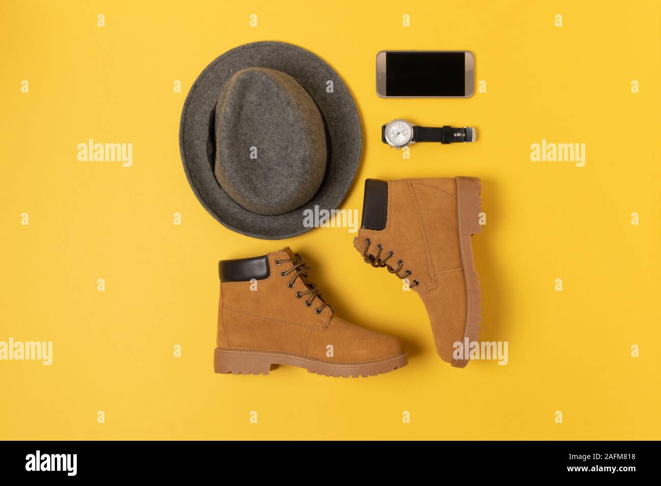 Layout der Herbst Kleidung und Accessoires in warmen Farben auf einem gelben Hintergrund. Hut, Stiefel, Telefon und schauen Sie sich flach in der Nähe. Stockfoto