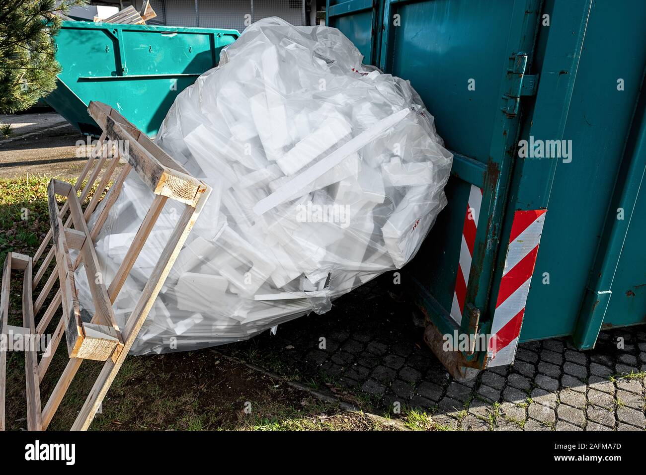 Grüne Behälter für Restmüll, eine große großen, durchsichtigen Plastiksack mit Styropor und eine hölzerne Palette lehnte sich gegen den Sack Stockfoto