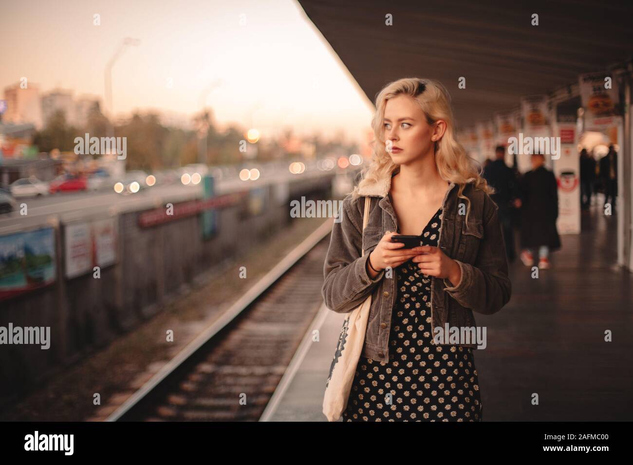 Junge nachdenkliche Frau mit Smart Phone beim Warten auf die Bahn Stockfoto