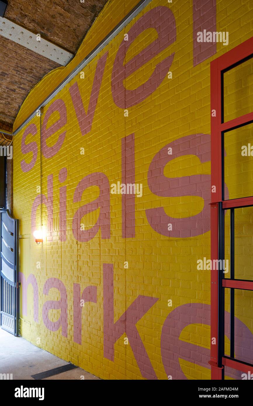 Grafik Schrift auf gelben Wand. Seven Dials Markt, London, Vereinigtes Königreich. Architekt: Steif+Trevillion Architekten, 2019. Stockfoto
