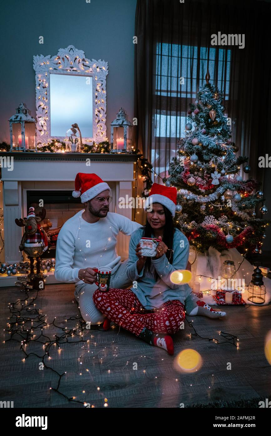 Nettes paar Weihnachtsbaum, Paar trinken heiße Schokolade unter dem Weihnachtsbaum vor dem Kamin im Wohnzimmer Stockfoto