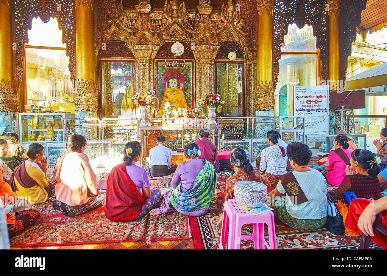 YANGON, MYANMAR - Februar 17, 2018: Die Gruppe der buddhistischen Anhänger auf das Gebet in Bild Haus der Sule Pagode, sitzen auf dem Boden vor der Budd Stockfoto