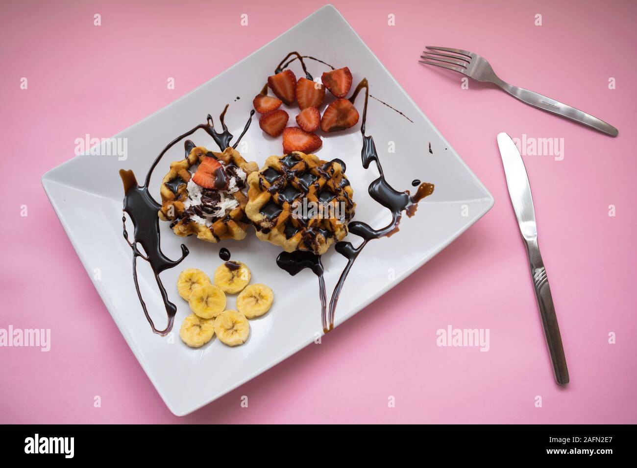 Waffeln mit Schokolade Sirup, Erdbeeren und Bananen auf einer Platte auf einem rosa Hintergrund Stockfoto