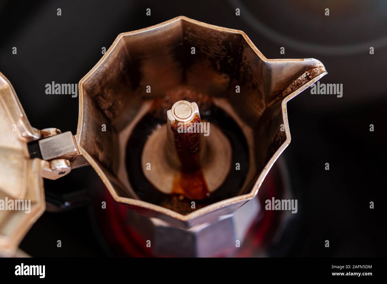 Prozess der Zubereitung von frischem Kaffee in einem Mokka Topf auf einem roten Warmhalteplatte: Kaffee ist steigend und fließt in den Topf, Nahaufnahme, selektiver Fokus, horizontal Stockfoto