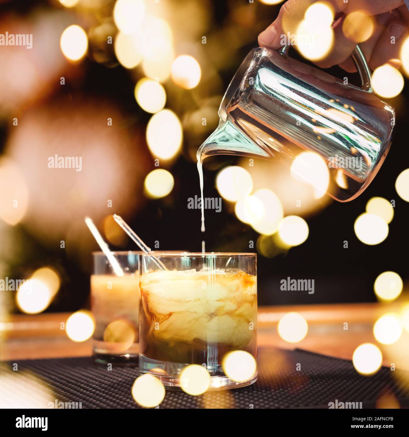 Vorbereitung von White Russian Cocktails auf der Theke auf Gummimatte. Flache DOF und Marsala tonned mit festlichen Bokeh leuchtet Stockfoto