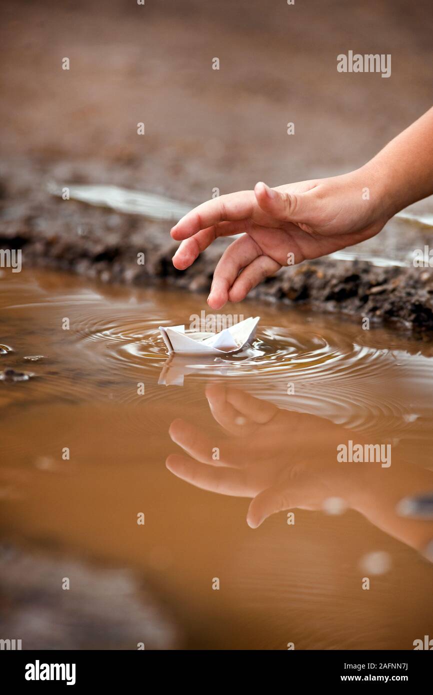 Nahaufnahme der Hand des kleinen Jungen spielen mit Papier Boot in der Pfütze. Stockfoto