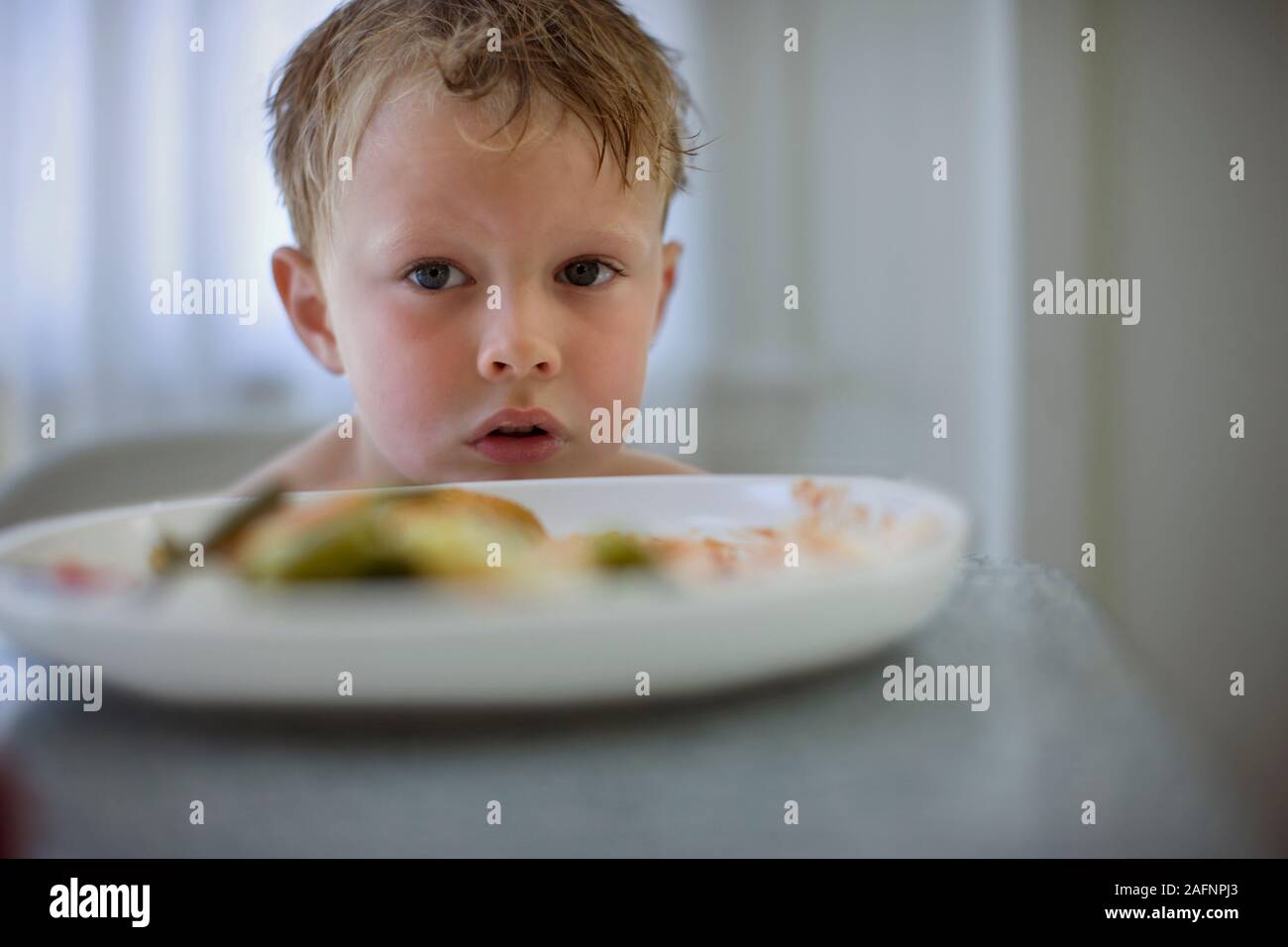 Junge sitzt an einem Tisch mit einer Platte von Lebensmitteln vor ihm. Stockfoto