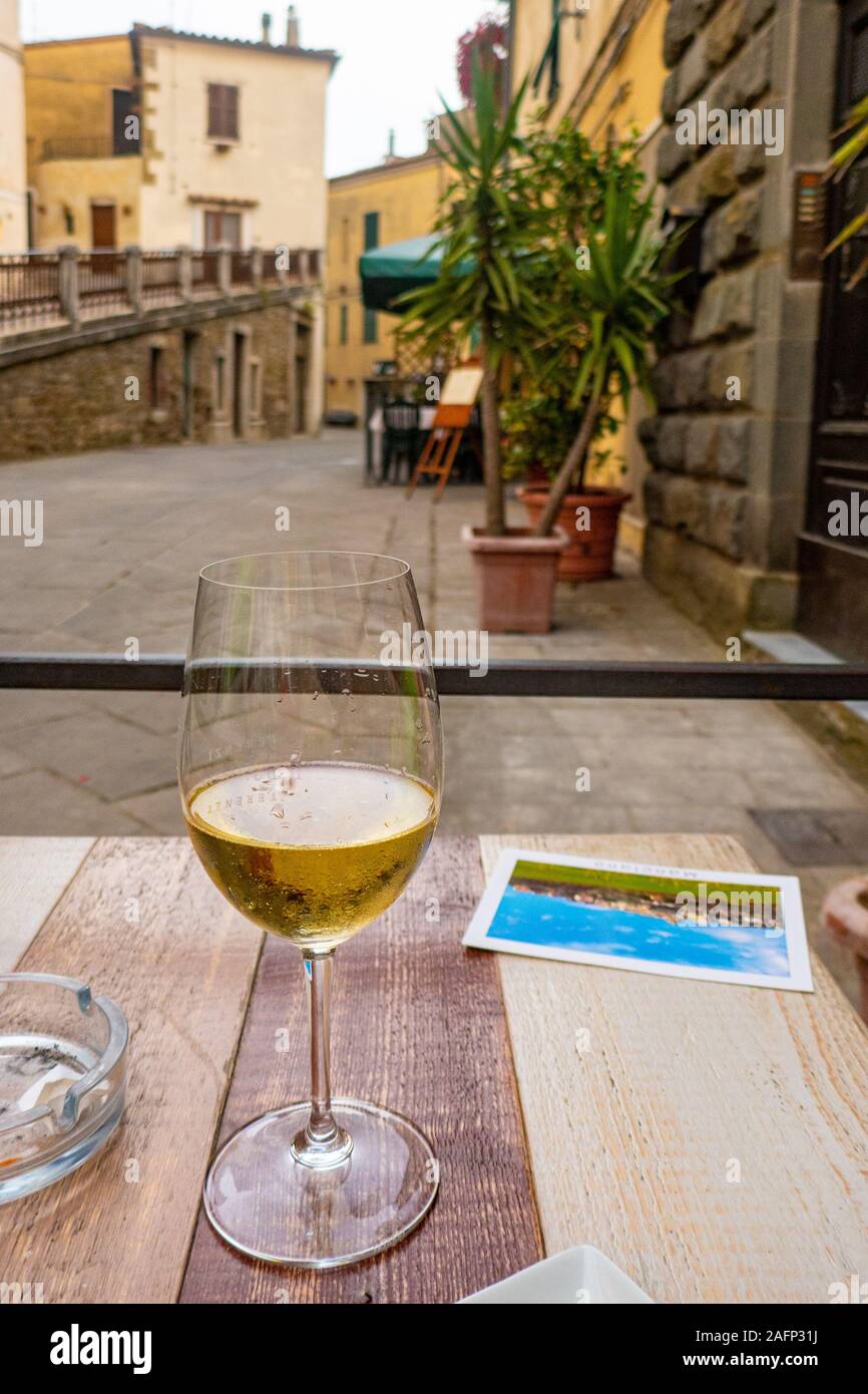 Ein Glas Weisswein mit einer Postkarte auf einem Tisch in einer typisch italienischen Straße Stockfoto