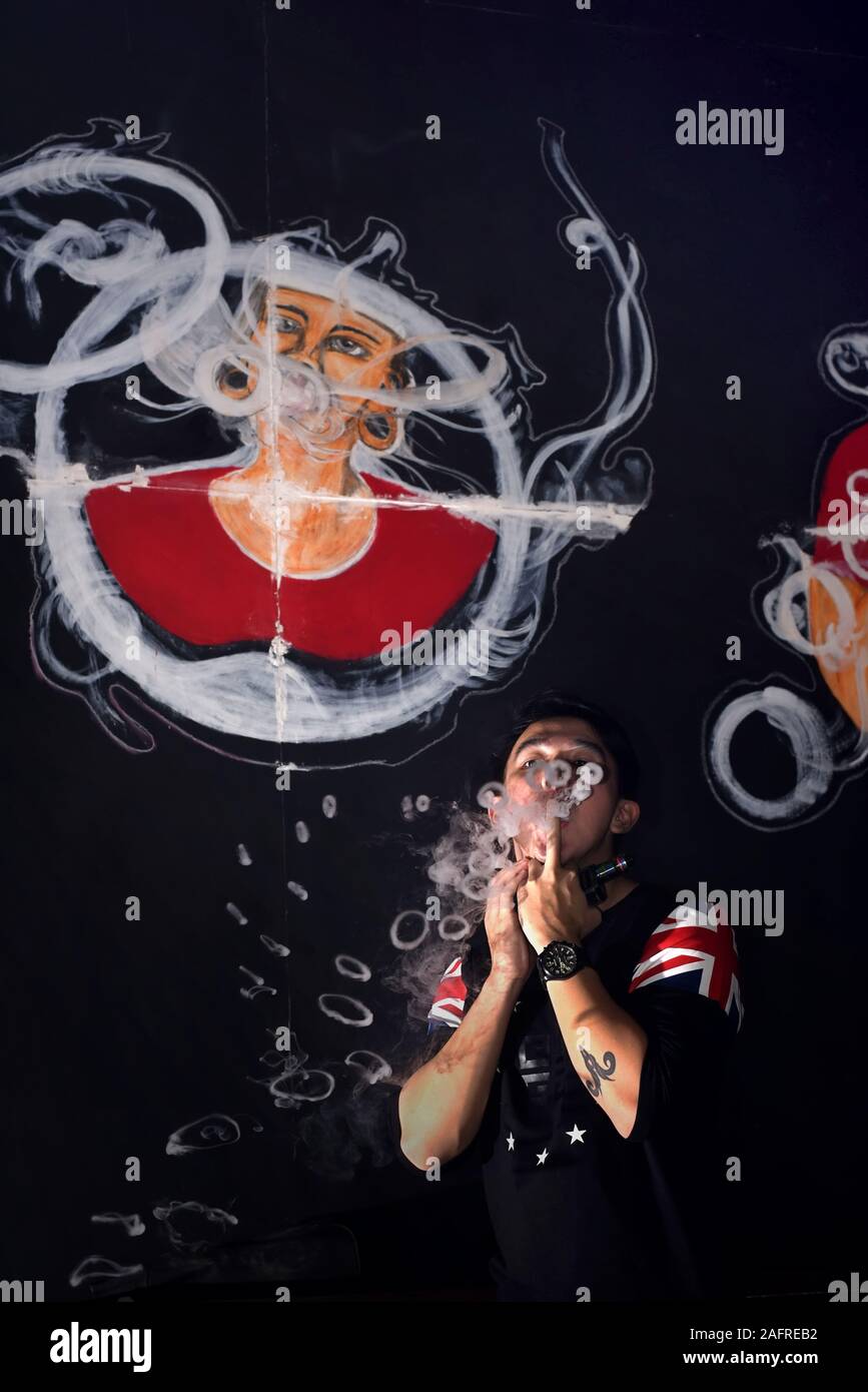 Osel Chandra, 21, zeigt einige seiner Vape Cloud Tricks vor den Wandmalereien eines Vape Shops. Stockfoto