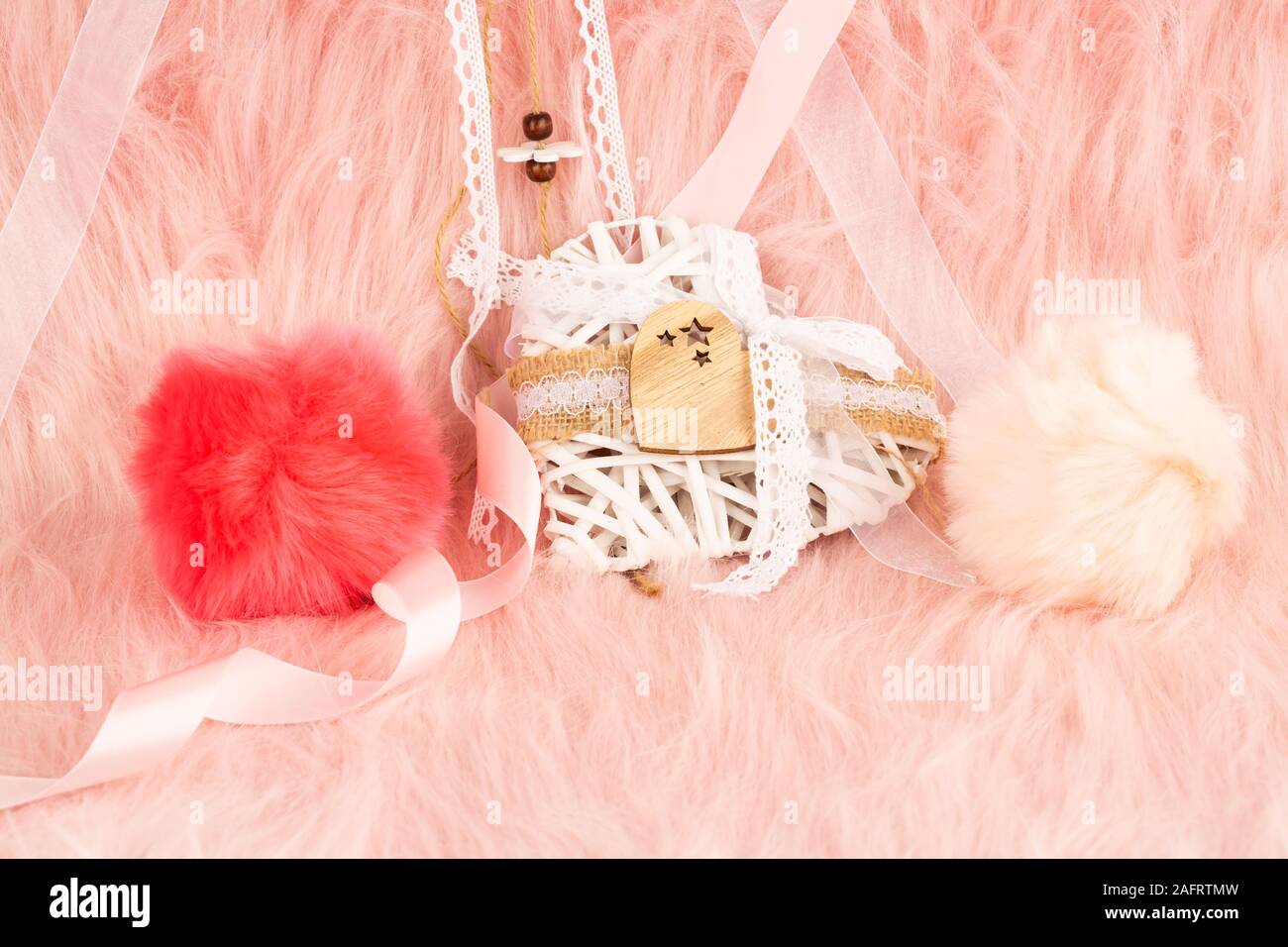 Weiße hölzerne Herz mit Schleife und flauschige Kugeln auf Pelz Hintergrund. Stockfoto