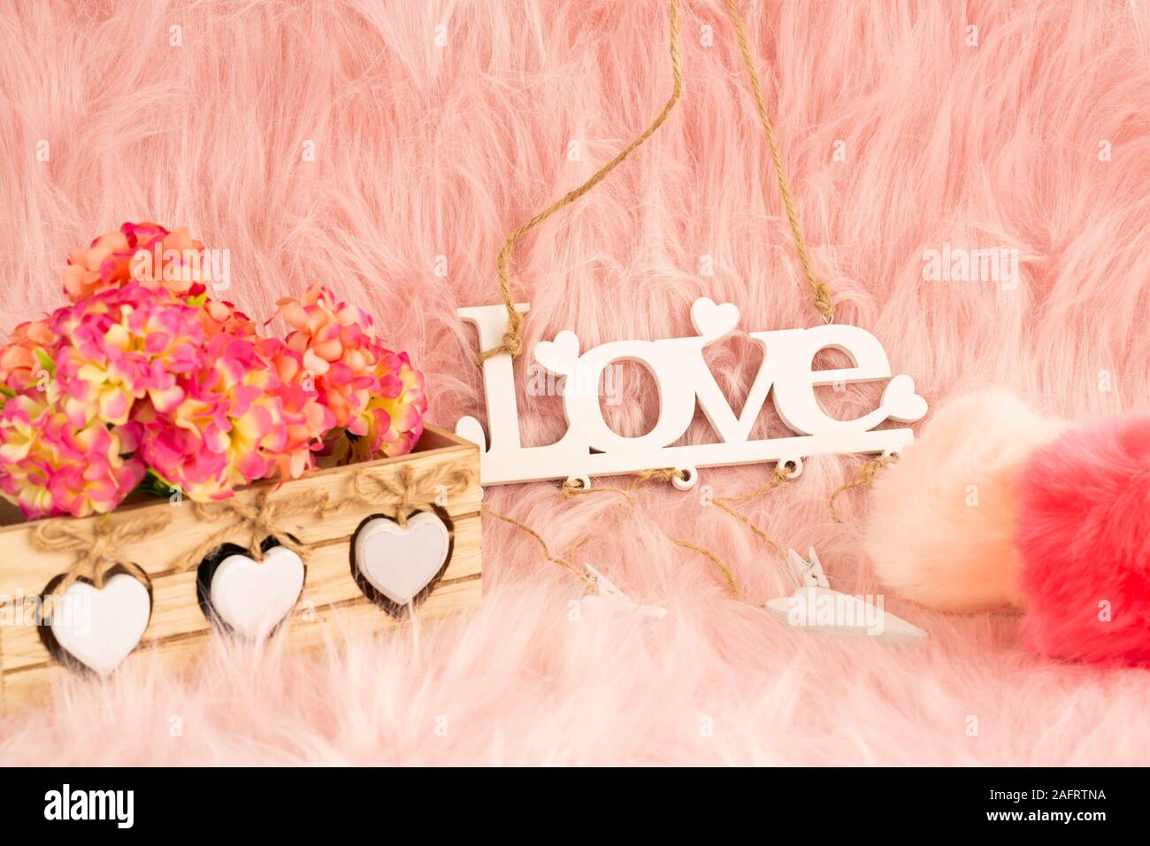 Weiß Holz- Wort Liebe, Box, Blumen und flauschige Kugeln auf Pelz Hintergrund. Stockfoto