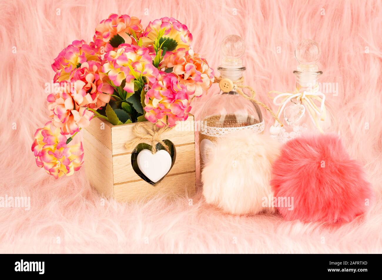 Beige Holzkiste, Blumen, Flaschen und flauschige Pompons auf Pelz Hintergrund. Stockfoto