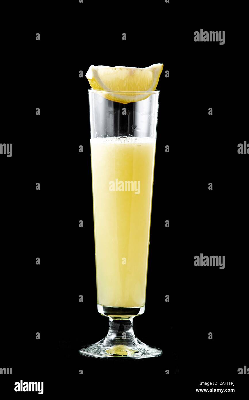 Frisch gepressten Zitronensaft in ein Glas, oben auf dem Glas ist ein Stück frische Zitrone. Auf schwarzem Hintergrund isoliert. Stockfoto