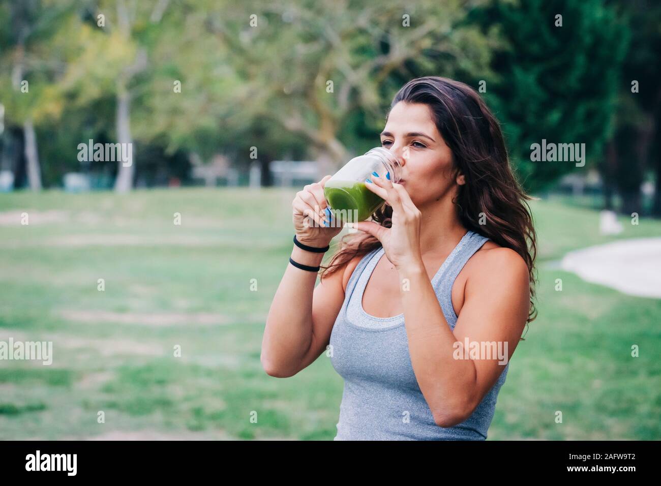 Passform weiblichen Personal Trainer trinken grünen Smoothie in Park Stockfoto