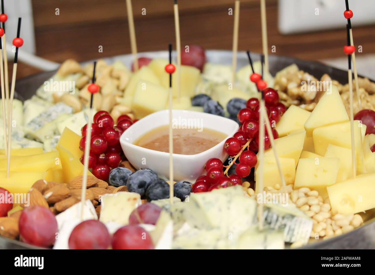 Platte mit Käse, Beeren und Nüsse auf der Party. Frische Snacks mit Holzstab und Sauce. Gesunder Urlaub gönnen. Food-fotografie. Rote Johannisbeere, Heidelbeere, Trauben-, Mandel-, Walnuß, Pinienkerne Stockfoto