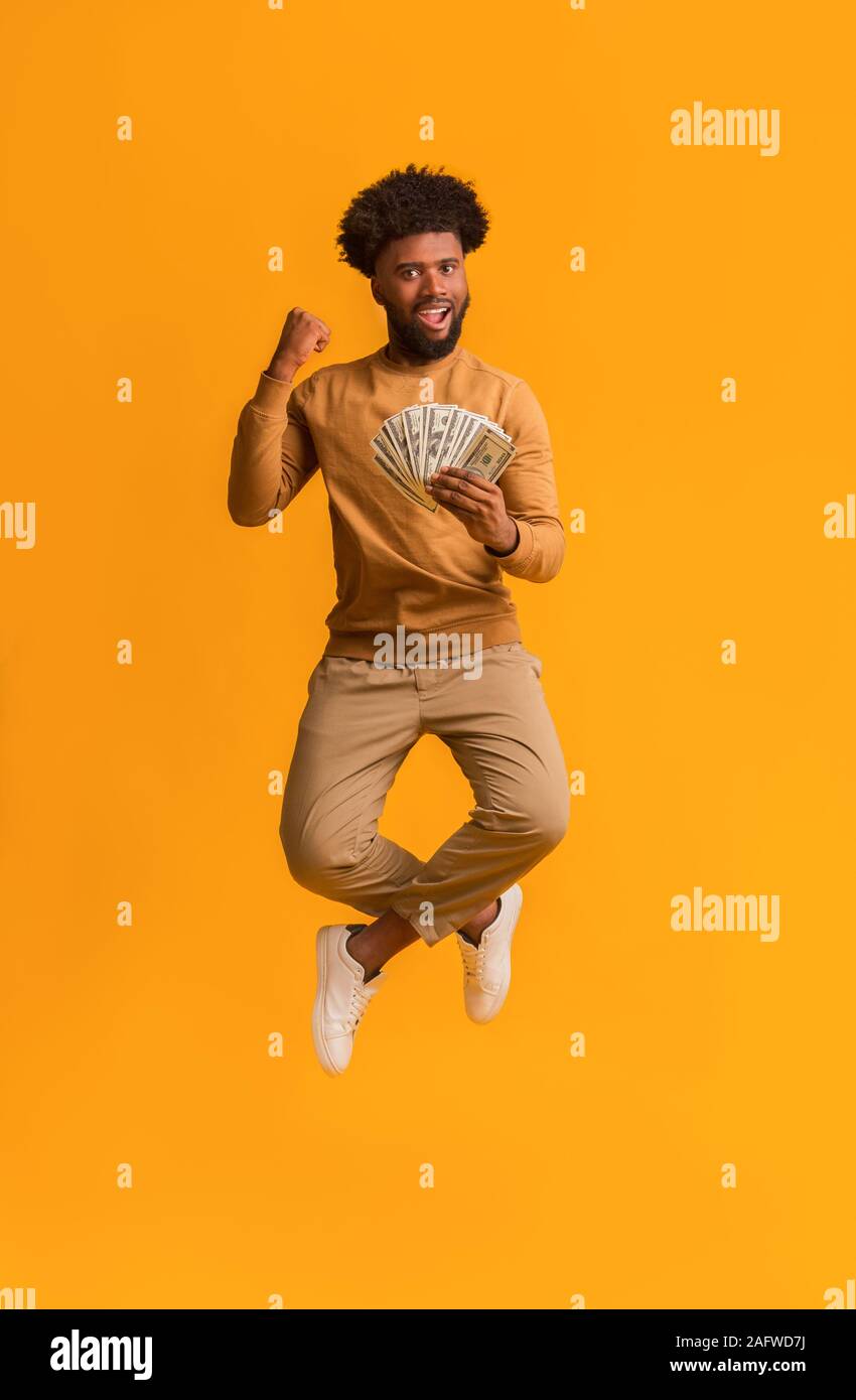Glückliche junge afro Mann springen mit Geld auf orangefarbenem Hintergrund Stockfoto