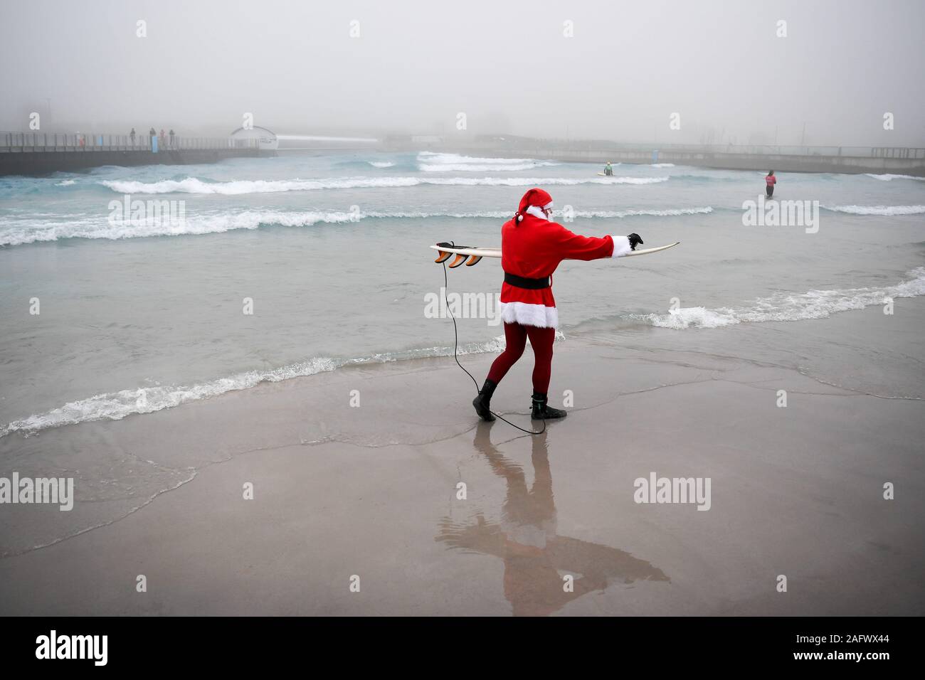 Ein Surfer in die festliche Stimmung als Santa gekleidet, wie er sich vorbereitet, die Wellen an das Landesinnere surfen Lagune an der Welle zu geben, in der Nähe von Bristol. Stockfoto