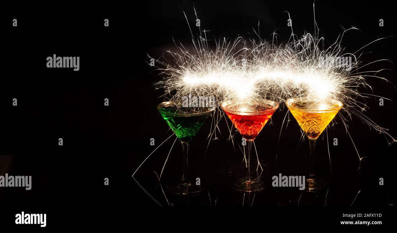 Realistische Aufnahme von drei bunten Cocktails mit Funkenlicht an Schwarzer Hintergrund Stockfoto