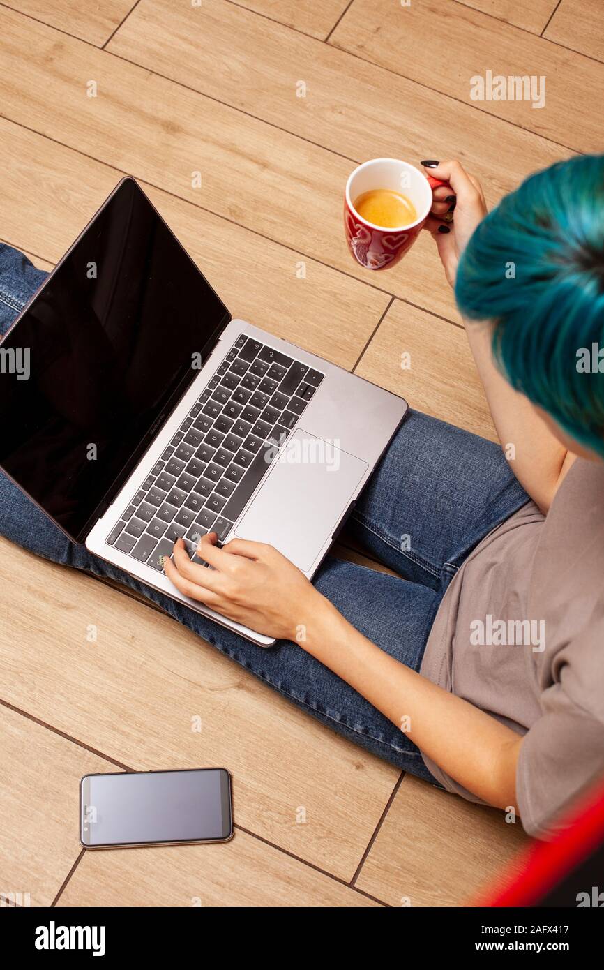 Mädchen mit Notebook und Tasse Kaffee sitzt auf dem Boden Stockfoto
