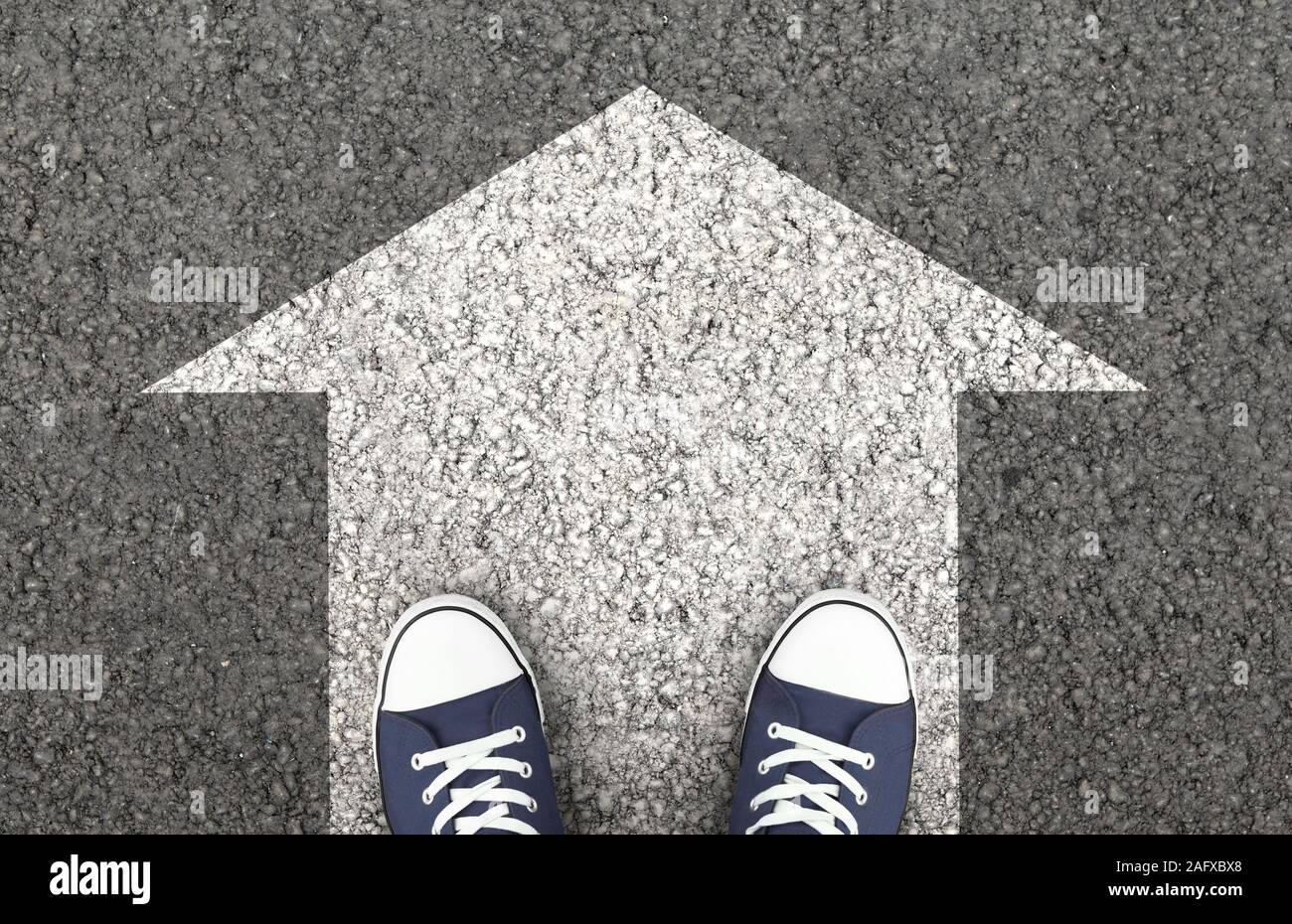 Blaue Schuhe auf der Asphaltstraße mit Pfeil Stockfoto