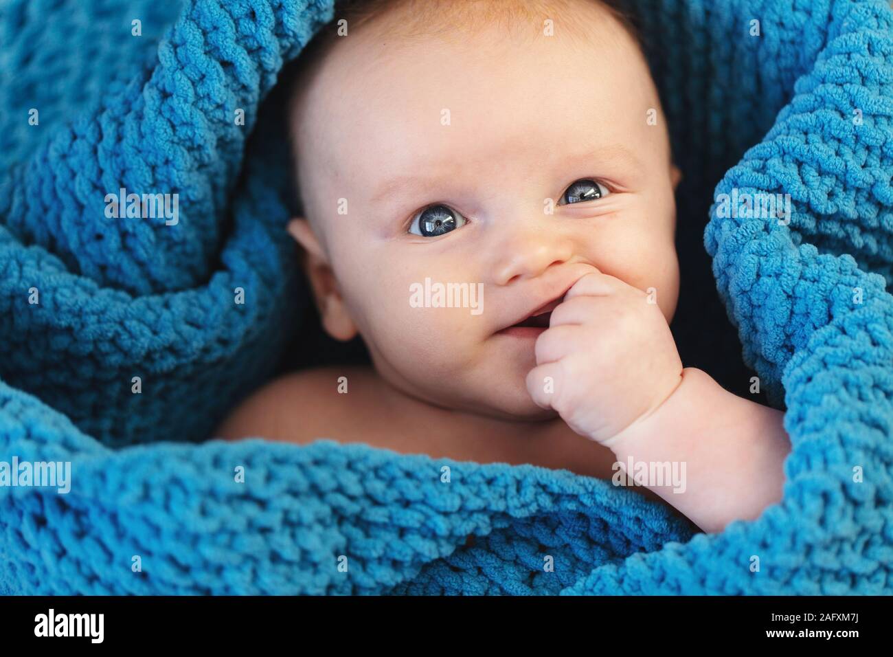 Ein niedliches Baby boy in einer gemütlichen blauen Decke in die Kamera schaut gewickelt Stockfoto