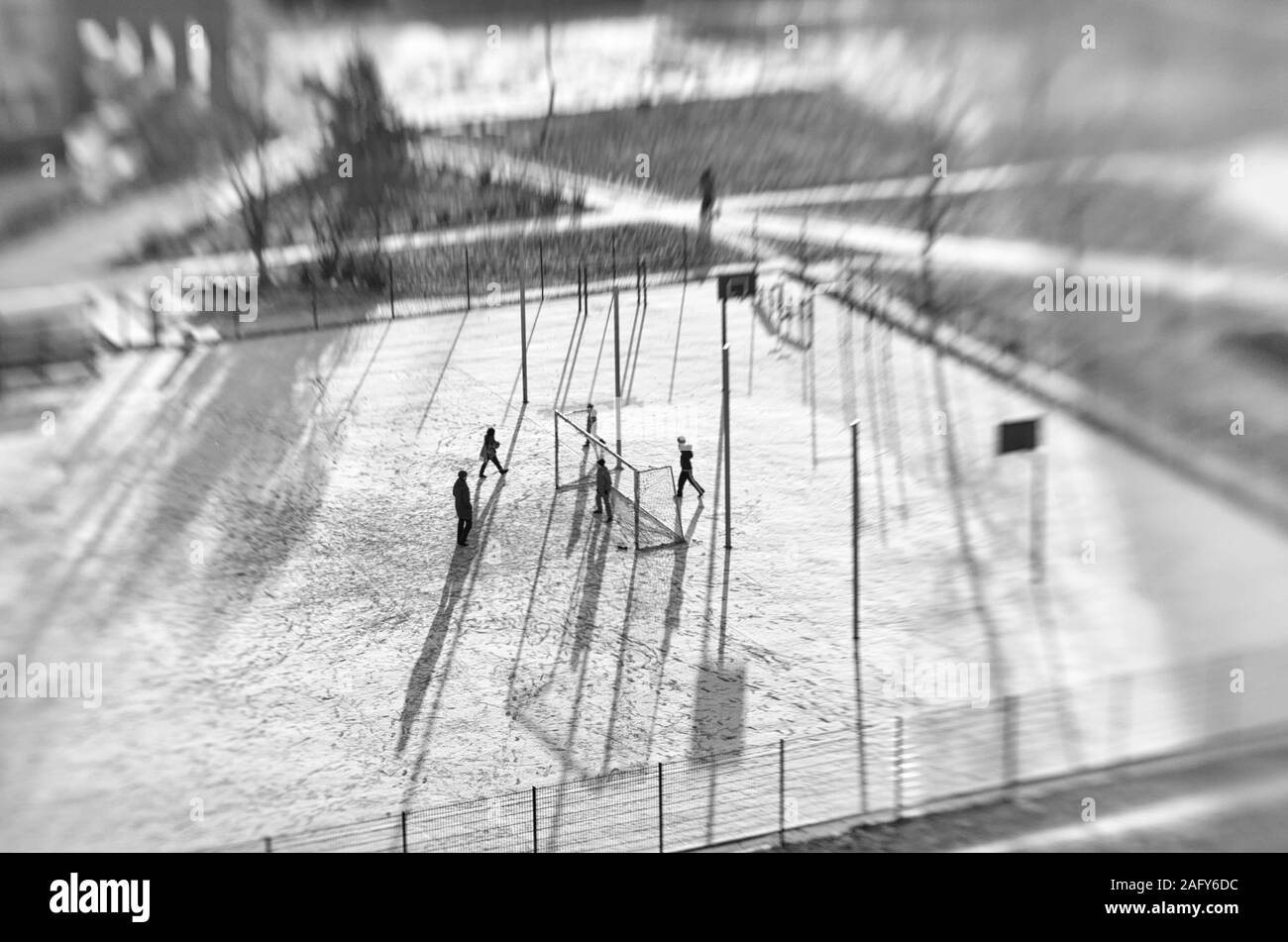 Nicht identifizierte Kinder und ein Erwachsener in der Ferne spielen Fußball in ein schneebedecktes Stadion in der Sonne Tilt Shift Effekt in der schwarz-weiss Stil Stockfoto