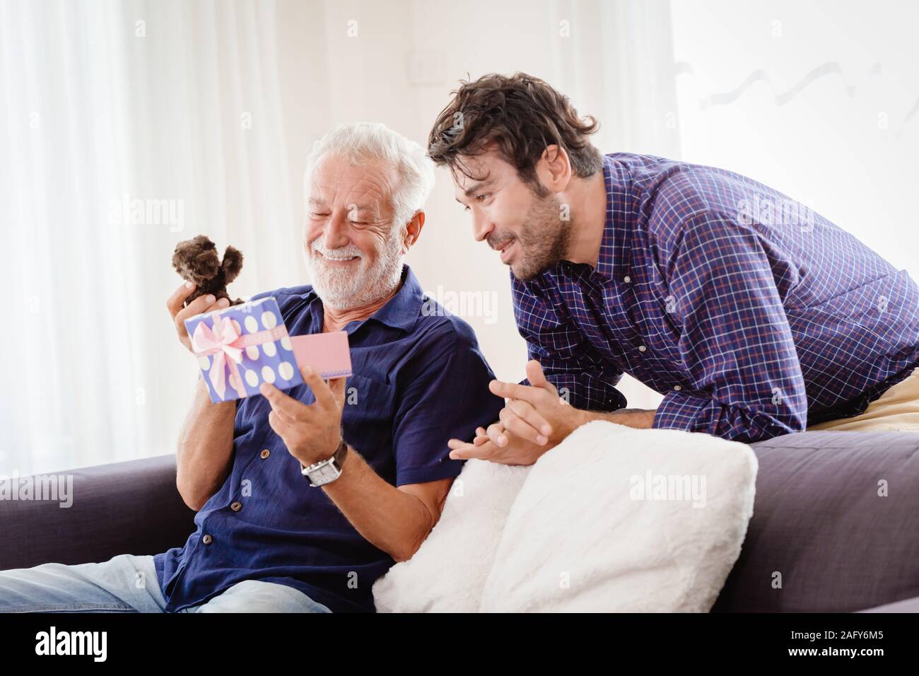 Junge Mann kehrte Familie zu Hause während Urlaub das Neue Jahr mit einer niedlichen Geschenkbox zu dem alten Mann, dem ältesten lächelte und war sehr zufrieden mit Teddy vorhanden. Stockfoto Junge Mann kehrte Familie zu Hause während Urlaub das Neue Jahr mit einer niedlichen Geschenkbox zu dem alten Mann, dem ältesten lächelte und war sehr zufrieden mit Teddy vorhanden. Stockfoto