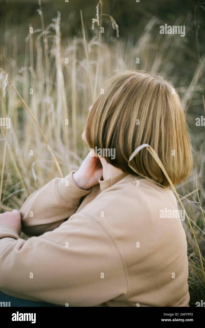 Porträt einer 40 Jahre alten Frau sitzt auf trockenem Gras im Freien Stockfoto