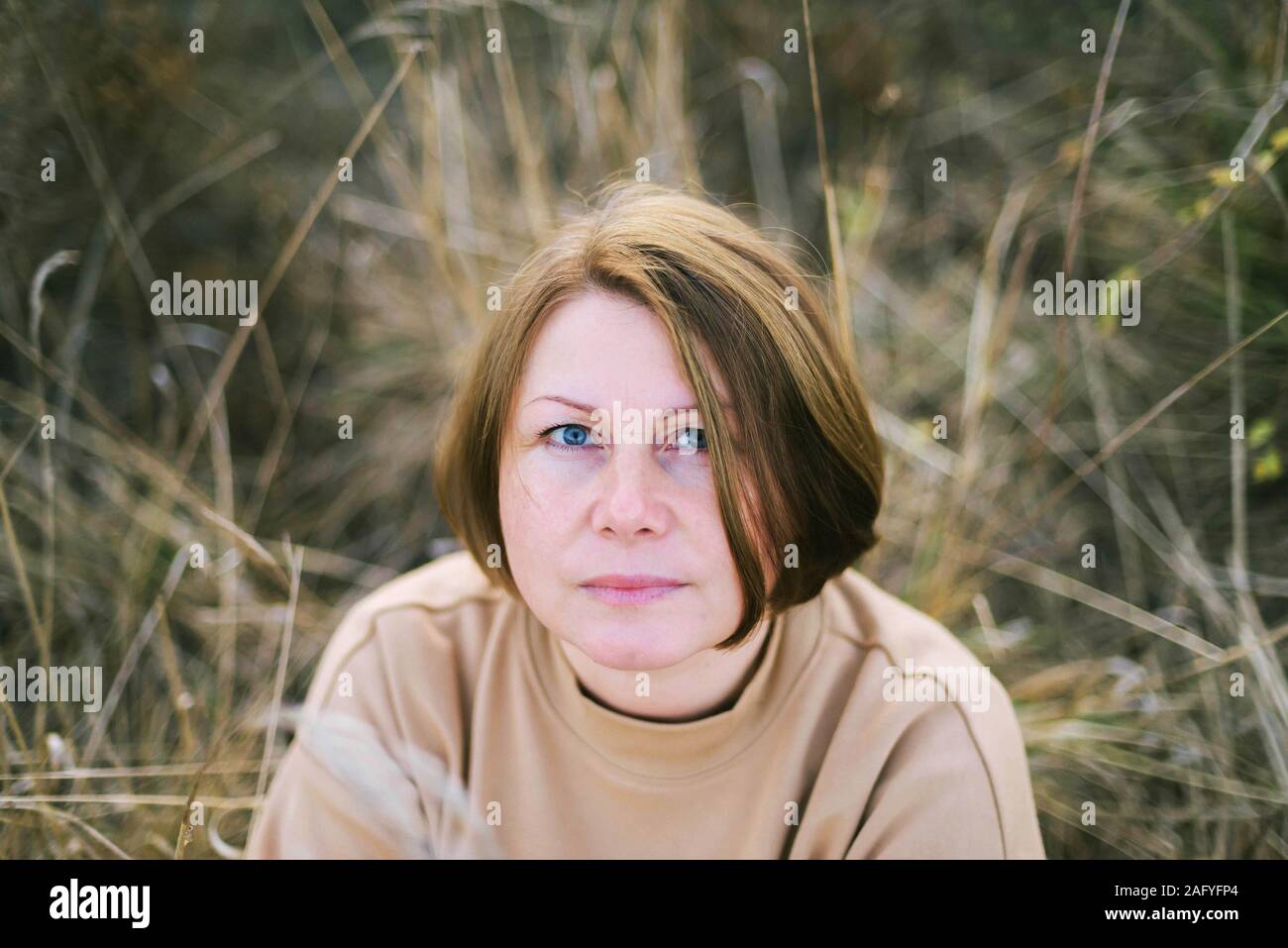 Porträt einer 40 Jahre alten Frau sitzt auf trockenem Gras im Freien Stockfoto