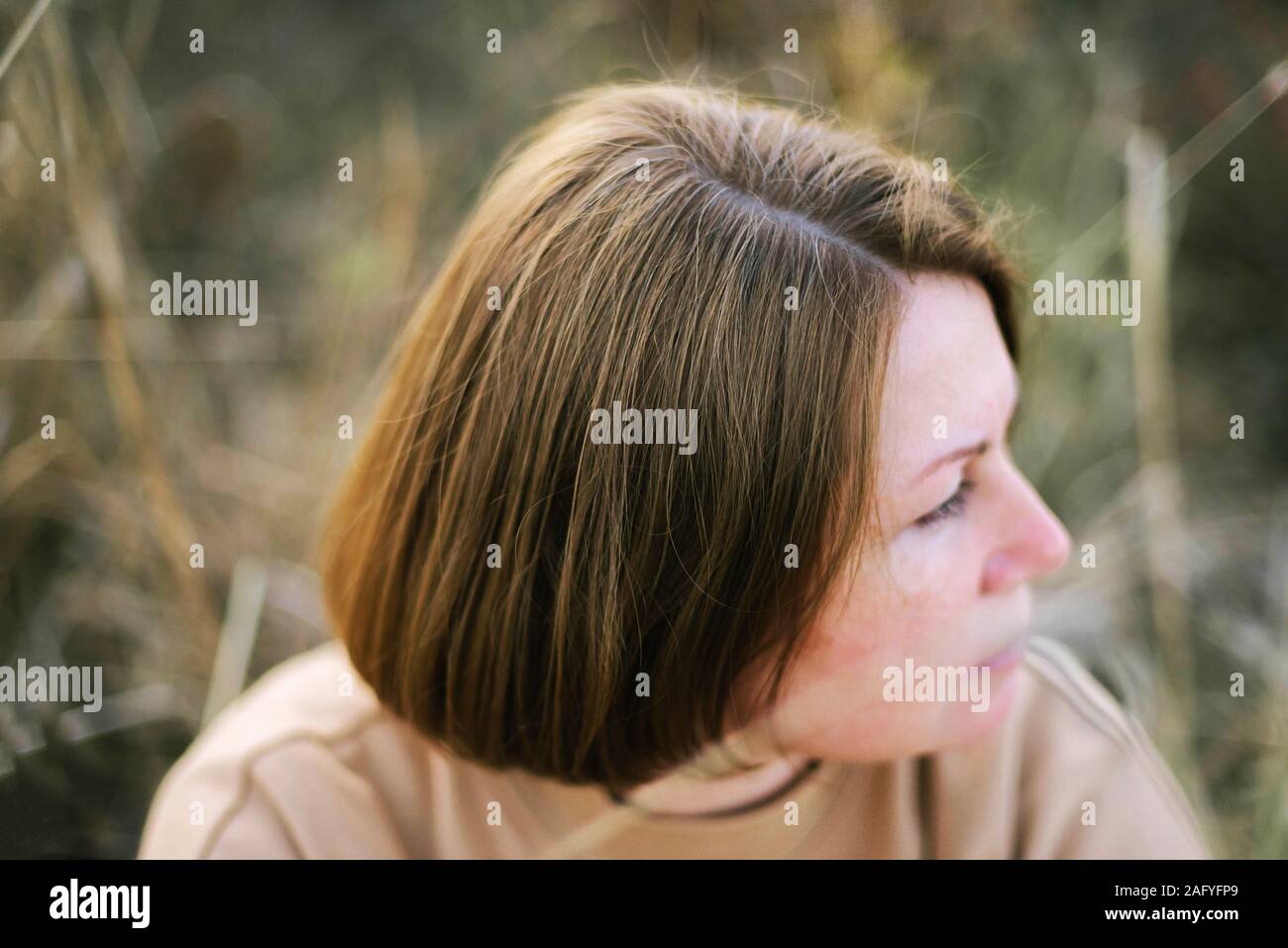Porträt einer 40 Jahre alten Frau sitzt auf trockenem Gras im Freien Stockfoto