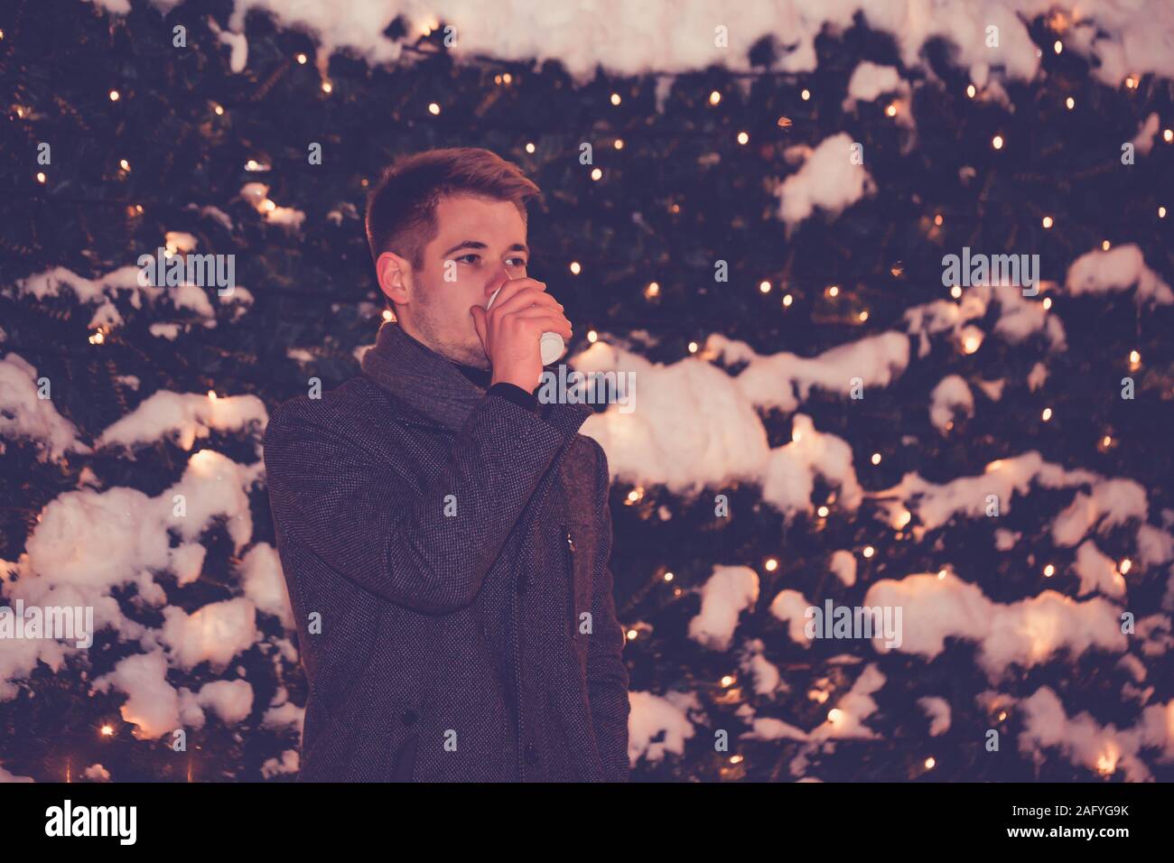 Night scene Portrait des jungen Mannes beim trinken Glühwein mit winter nacht Lichter im Hintergrund Stockfoto
