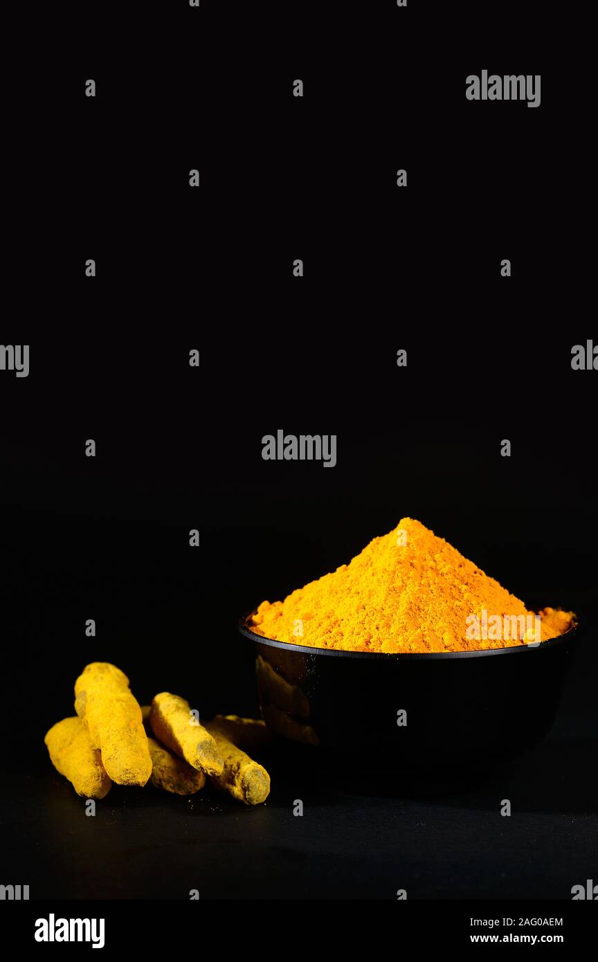 Kurkuma Pulver und Wurzeln oder Rinden in schwarz Schüssel auf schwarzem Hintergrund Stockfoto