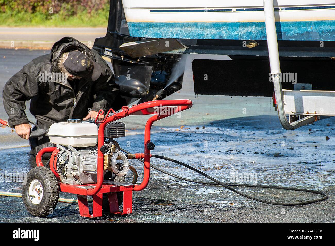 Mann Reinigung unter Boot mit Hochdruckreiniger Ausrüstung Stockfoto